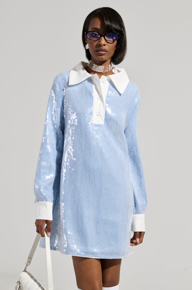 A person wearing the stylish Chic AF Sequin Poplin Mini Dress, featuring a light blue and white pinstripe pattern with a white collar and cuffs, complemented by sunglasses, a choker necklace, and carrying a white handbag.