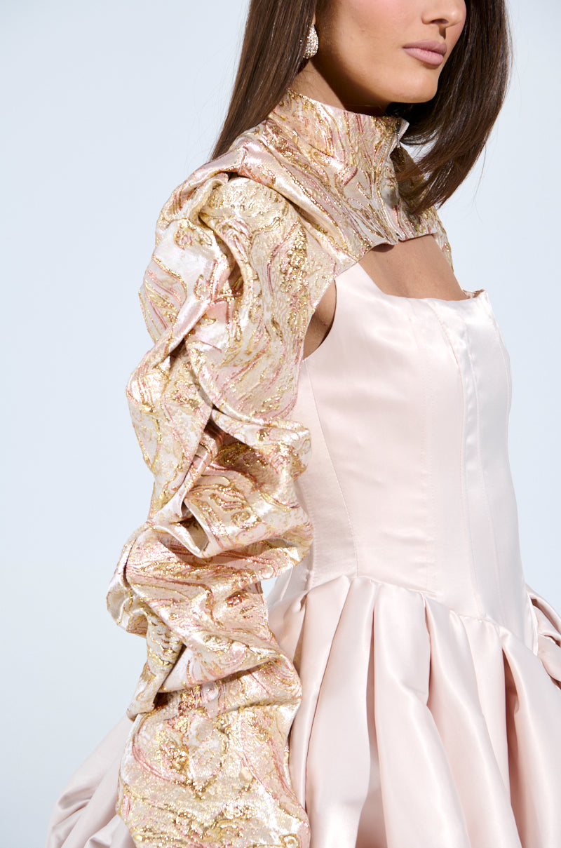 The woman exudes a party-ready elegance in her CORA BROCADE BOLERO, featuring gold and pink floral brocade with a corset bodice and ruffled sleeves. Her straight brown hair and teardrop earrings enhance the sophisticated look in the photo cropped at her nose and hips.