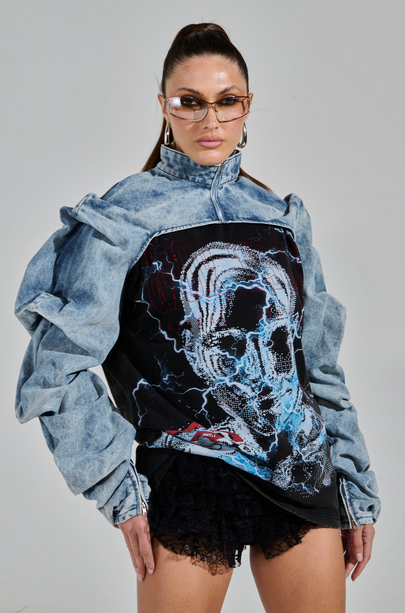 A person confidently rocks the SPOIL ME DENIM BOLERO, which features an ultra-cropped fit and voluminous sleeves. They pair it with a graphic design shirt, sunglasses, hoop earrings, and have their hair in a sleek high ponytail.