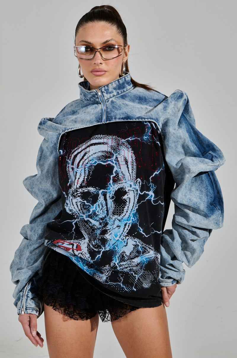 A person is wearing the SPOIL ME DENIM BOLERO over a graphic print top with a futuristic skull design. They have long hair pulled back and are wearing sunglasses against a plain gray background.