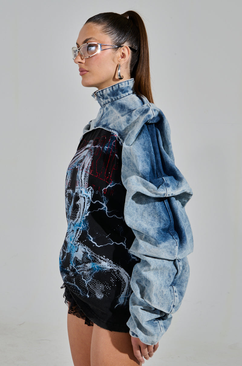 Against a plain background, a person with long hair styled in a high ponytail wears the unique SPOIL ME DENIM BOLERO featuring ruched detailing and pairs it with a black graphic top, large hoop earrings, and rectangular glasses.