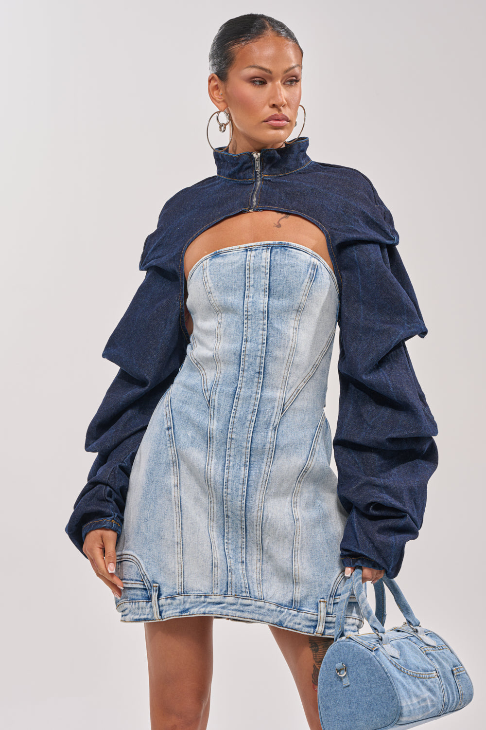 A woman flaunts street-style flair in a strapless light denim mini dress, layering with the SPOIL ME BOLERO IN DARK DENIM and carrying a small denim handbag for a chic finish. 1