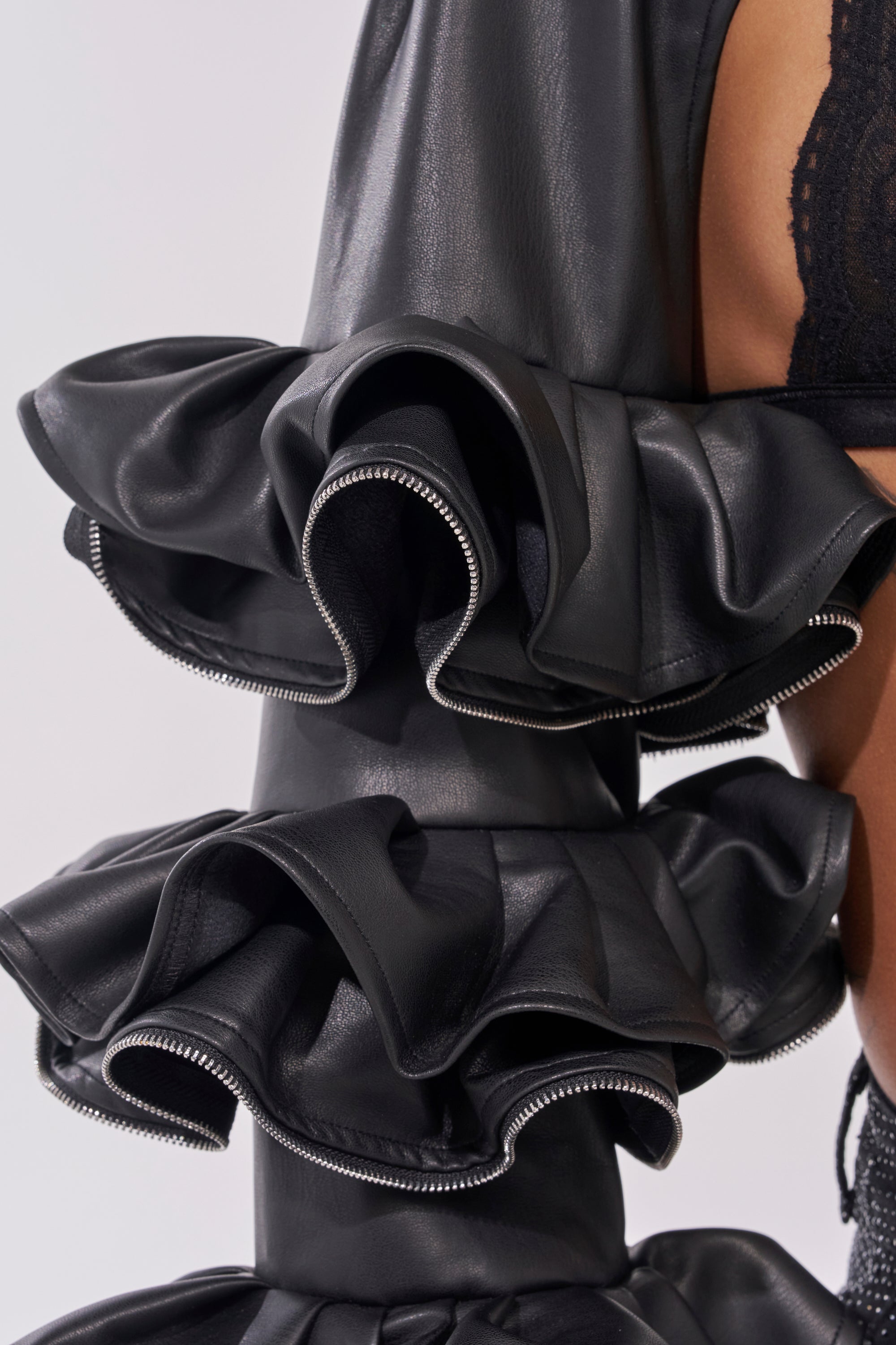 Close-up of the DON'T MESS RUFFLE BOLERO in black faux leather, featuring ruffle sleeves and exposed silver zippers. Lace fabric and bare skin are visible in the background. 8