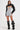 Dressed in the stunning CORA CRINKLE PU BOLERO, a woman exudes confidence in a metallic mini dress highlighted by circular cutouts and crinkle faux leather, complete with ruched sleeves. She complements the chic ensemble with tall, slouchy black boots set against a plain white backdrop.