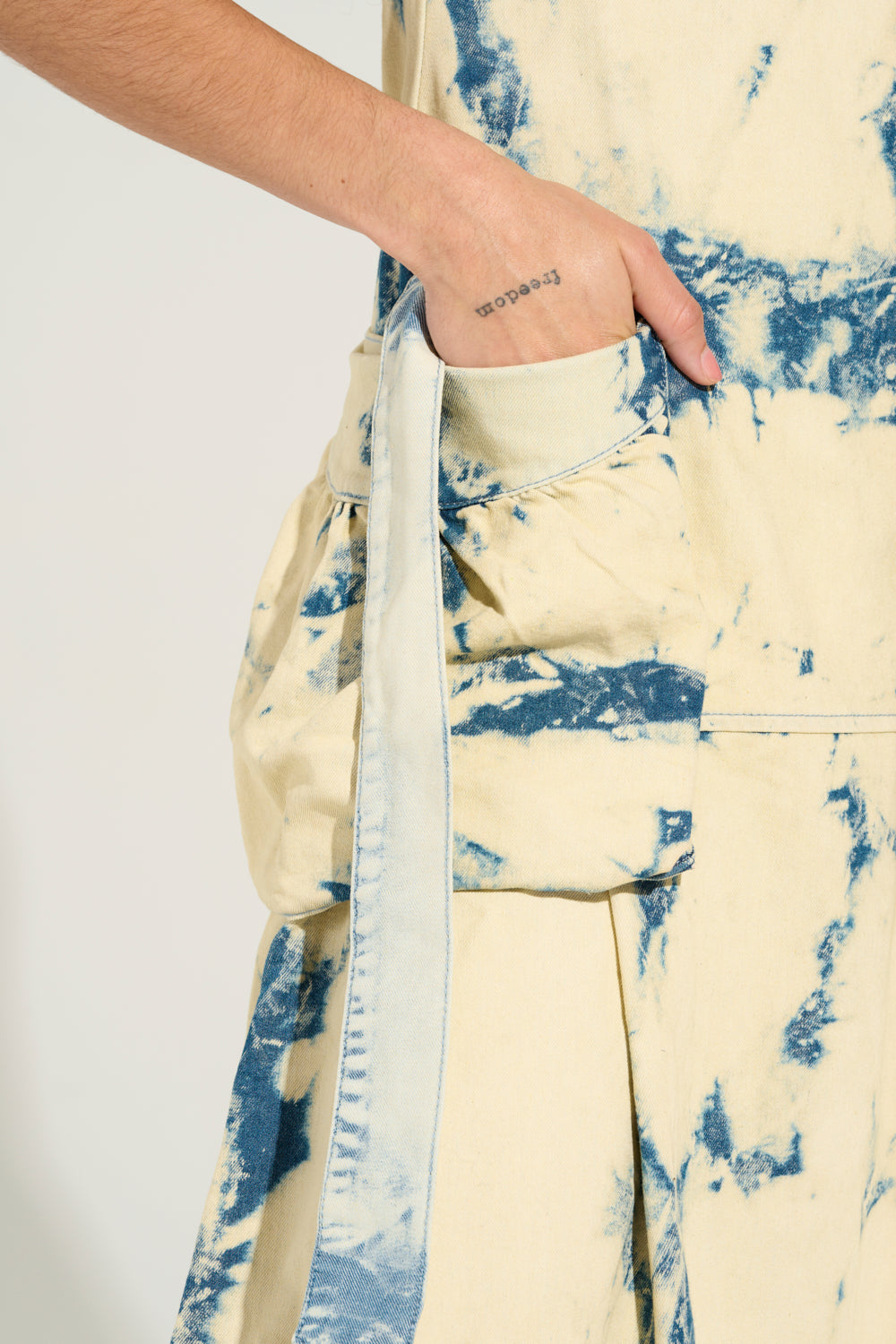 A person wearing the STREET STYLE ACID WASH MAXI DRESS, featuring vibrant blue and white patterns, casually has their hand in a pocket. Their street style is further highlighted by a small tattoo of the word "someday" on their arm, blending effortlessly with the maxi dress's dynamic look.