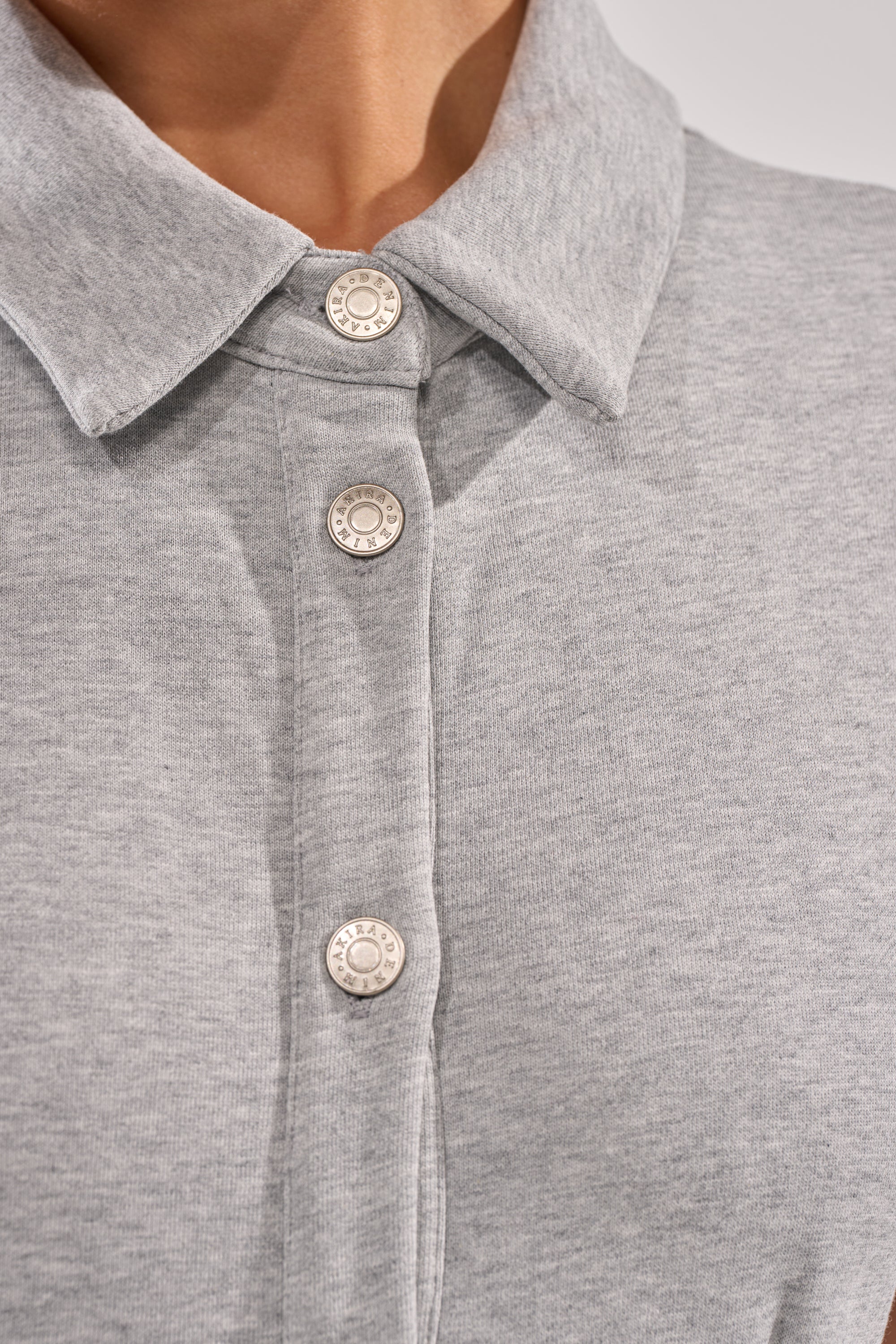 Close-up of a person wearing the AVERY SHORT SLEEVE FRENCH TERRY MINI DRESS in heather grey, featuring a soft, textured fabric, collared neckline, and three white buttons. Only the neck and upper chest are shown. 6