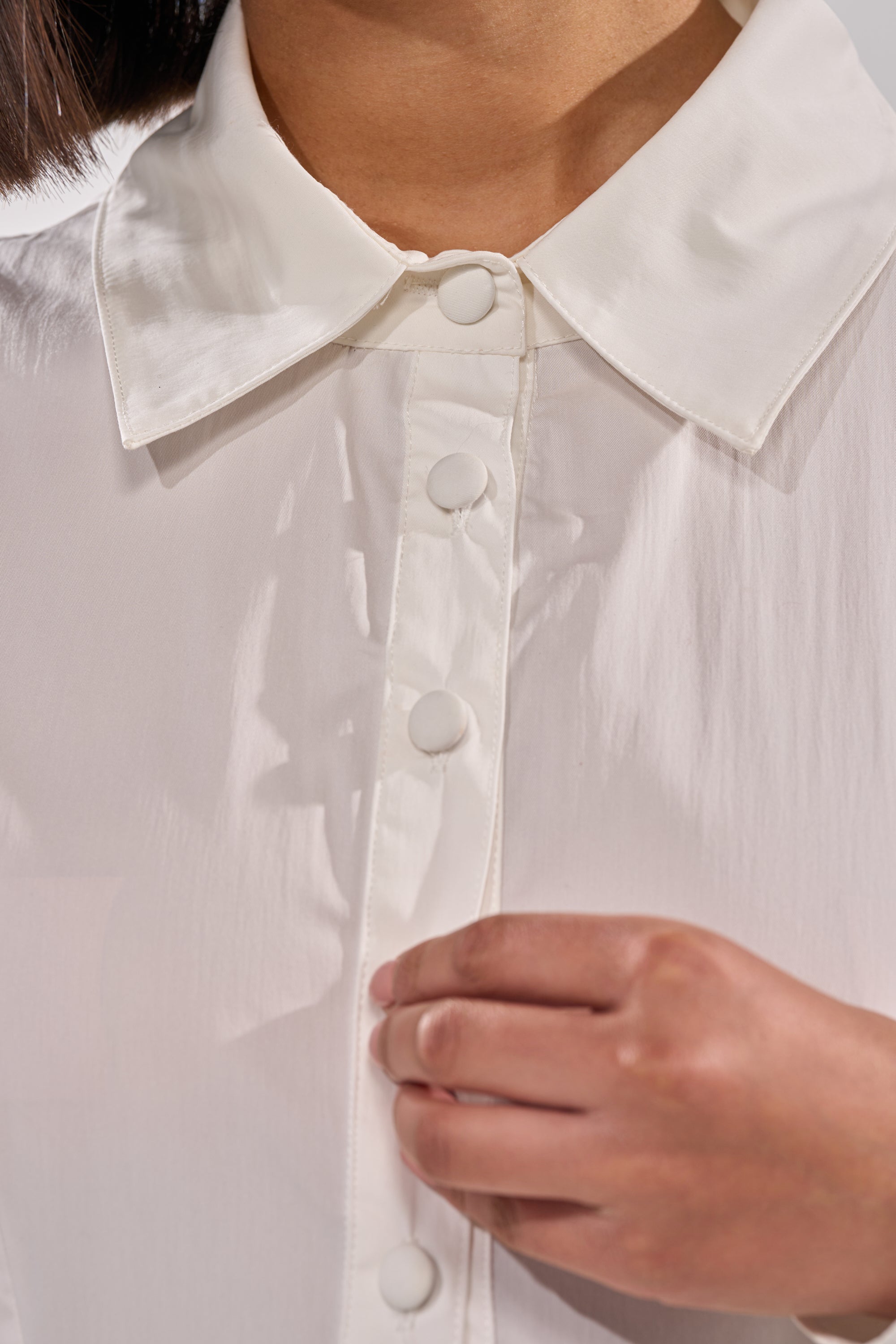 A close-up shows a person in THE IT GIRL POPLIN MINI DRESS, featuring a pointed collar and round buttons. Only the lower half of their face and one hand, gently touching near the buttons, are visible. 5