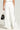 A person is standing in the DANCING IN THE DARK FRENCH TERRY WIDE LEG SWEATPANT featuring decorative chain details along the sides. They are holding a black handbag with white handles. The background is plain and light-colored, while the person's upper body is not visible.