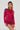 A person with long braided hair is wearing the IF LOOKS COULD KILL Rhinestone Mini Dress in red, showcasing a curve-hugging silhouette. Holding sunglasses, they strike a confident pose in the sparkly, fitted dress made from stretchy mesh knit against a plain background.