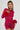 A person with braided hair poses confidently in the IF LOOKS COULD KILL RHINESTONE MINI DRESS IN RED. The curve-hugging silhouette, accented with red fur cuffs, sparkles brilliantly against the plain white background, showcasing a vibrant and unforgettable style.