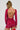 A person with braided hair is wearing the If Looks Could Kill Rhinestone Mini Dress in red, which accentuates their form with its curve-hugging silhouette. The sparkly backless design highlights multiple tattoos on their back as they hold a red feathered accessory against a plain background.