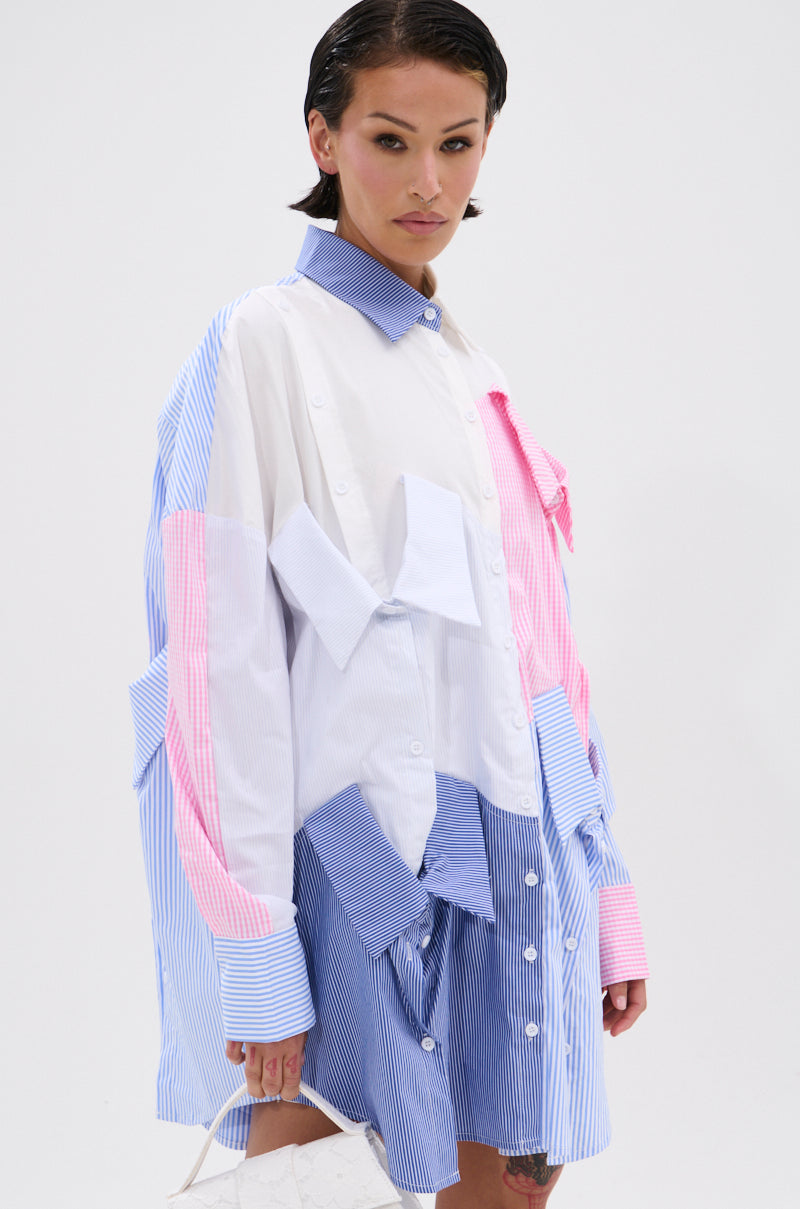 Wearing the MY BOYFRIENDS SHIRT POPLIN MINI DRESS with blue, pink, and white stripes, large pockets, and a bow detail, a person stands against a white background holding a small white handbag.