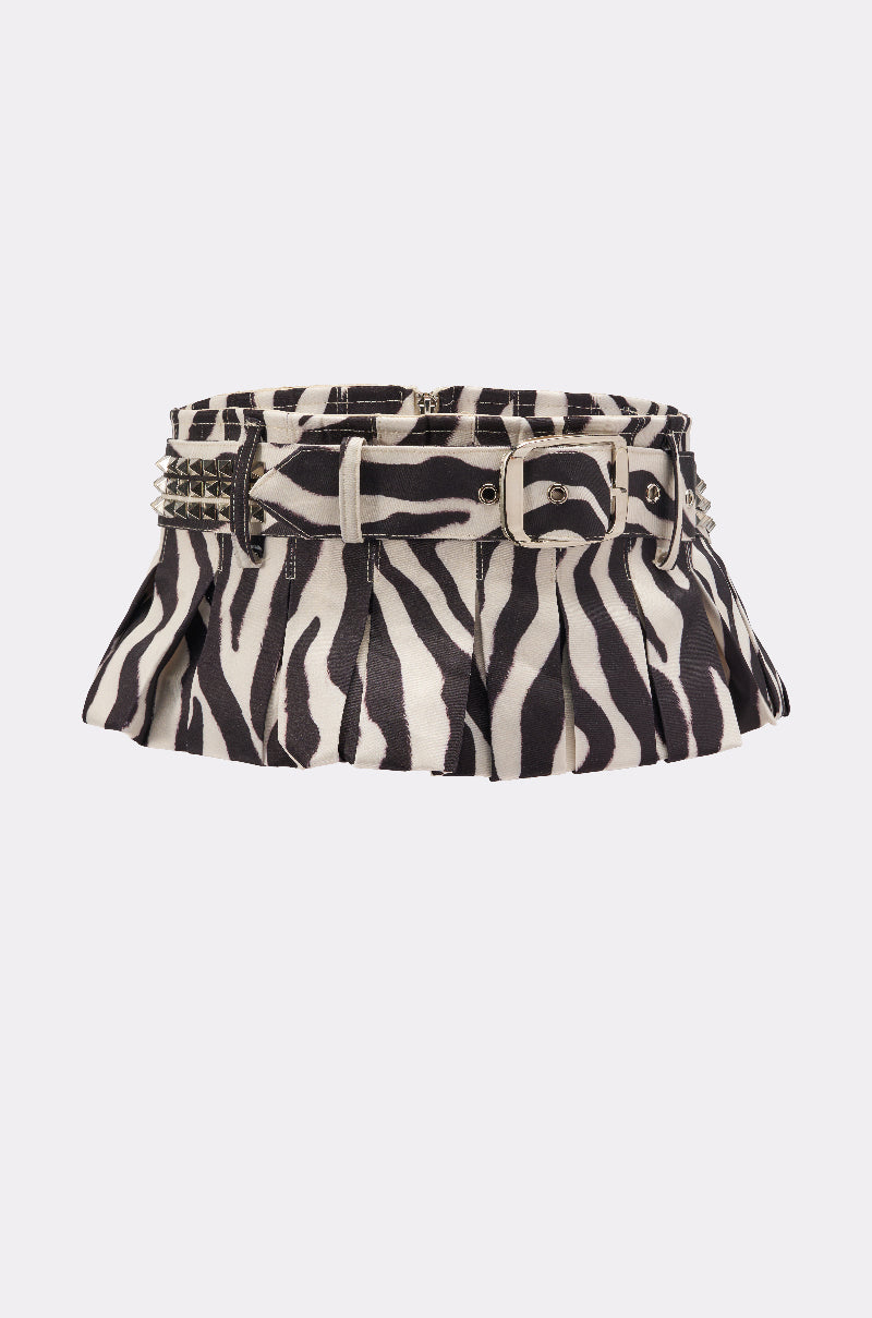 The ZEBRA PEPLUM BELT SKIRT is a pleated mini skirt with a black-and-white zebra print, featuring a matching belted waist with silver buckle and studs, shown against a plain white background.