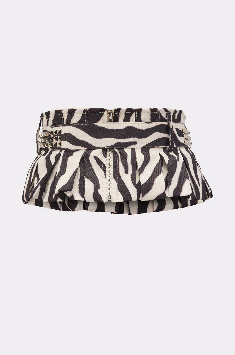 The ZEBRA PEPLUM BELT SKIRT features a black and white zebra print, ruffled hem, silver center zipper, metallic spike studs by the waistband, and an adjustable belt for added edge.