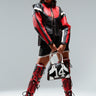 A model poses confidently in the ROCKY CORSET MOTO, a black and red quilted faux leather jacket, paired with matching high boots and a black mini skirt. She accessorizes with a black and white handbag featuring the number 14. The outfit boasts a futuristic, edgy design against a plain light gray background.