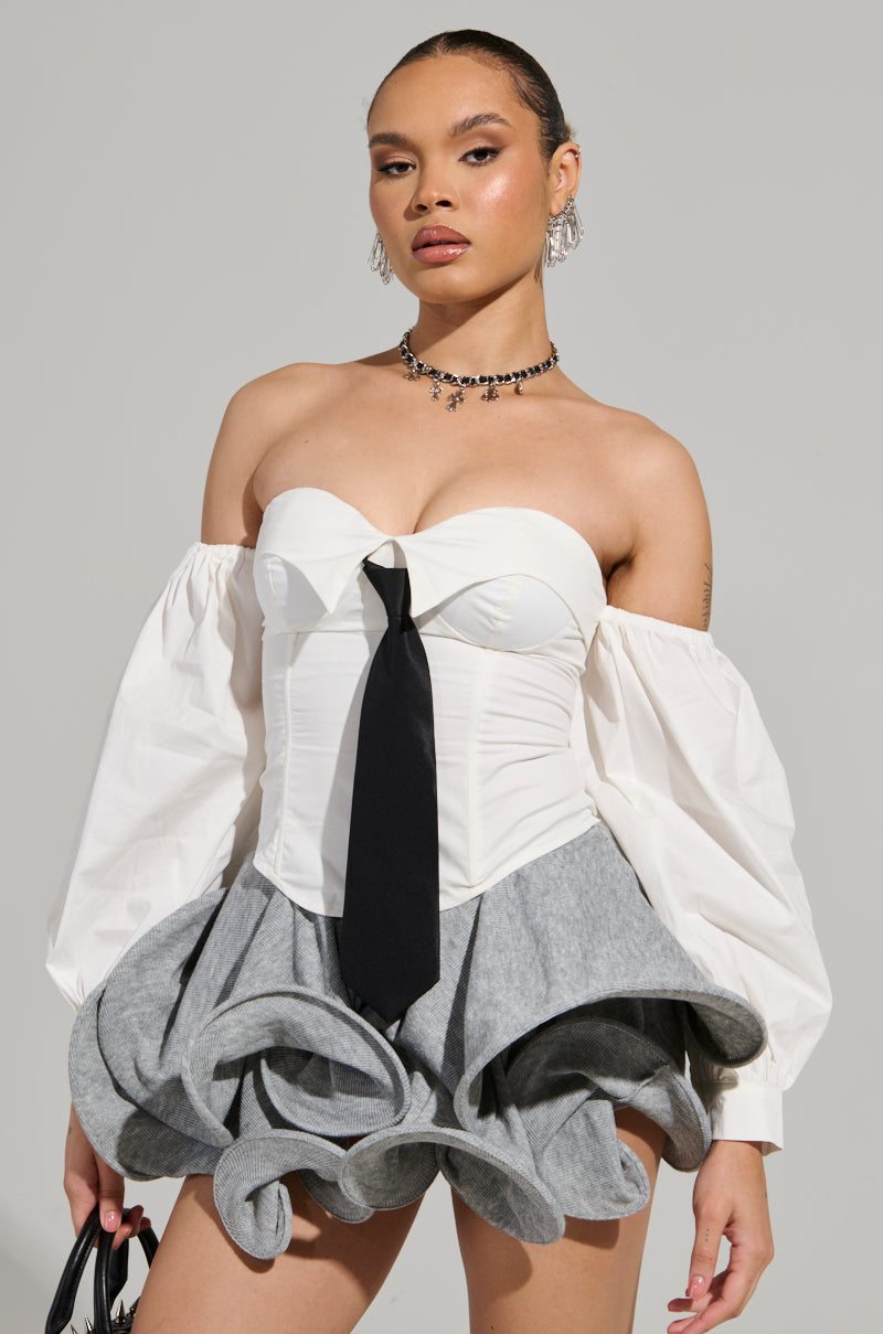 Dressed in the LETS DO IT BLOUSE, an individual exudes confidence with its strapless neckline corset and striking black necktie, accented by dramatic off-the-shoulder puffy sleeves. The ensemble is completed by a uniquely voluminous skirt with gray ruffles, complemented by earrings and a necklace for a bold look.