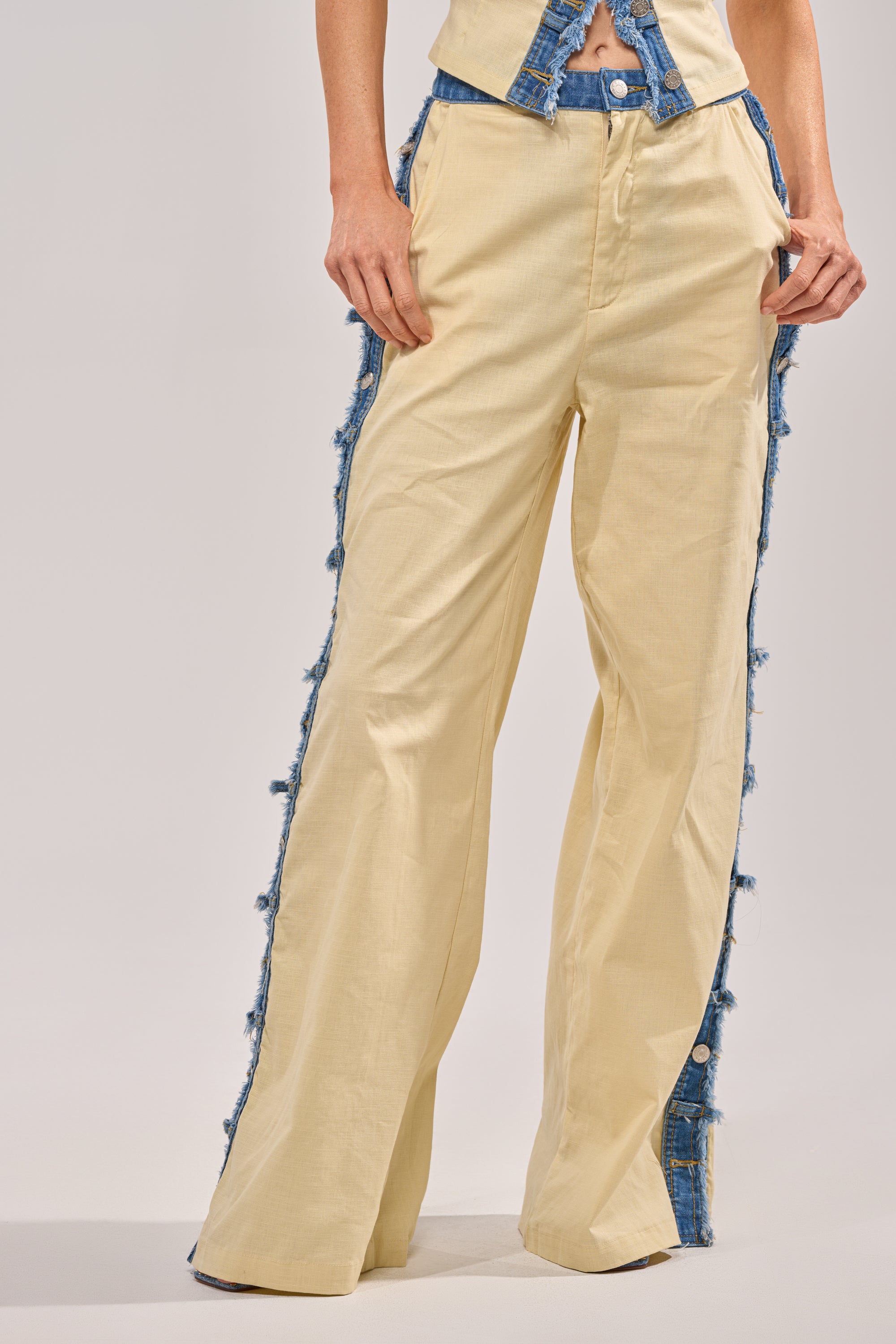 A person wearing the DO YOU LOVE ME TROUSER, which are high-waisted beige linen pants featuring a wide-leg silhouette and frayed blue denim trim on the sides. Only the lower half of their body is visible.