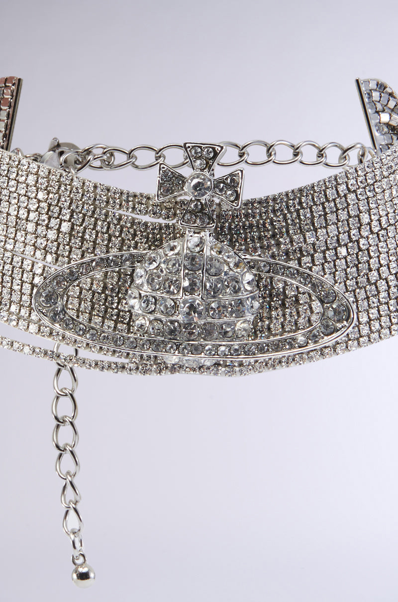 The TITI CHOKER NECKLACE showcases a broad array of radiant rhinestone chain links, highlighted by a central globe-shaped pendant encircled by a ring and topped with a cross embellished with smaller rhinestones. This elegant necklace is secured with an adjustable lobster clasp closure. 2