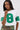 A woman with long straight hair and large hoop earrings poses with one hand near her face, wearing camouflage pants and the WINNERS ONLY RHINESTONE SHORT SLEEVE TEE featuring a sparkling green "8" graphic.