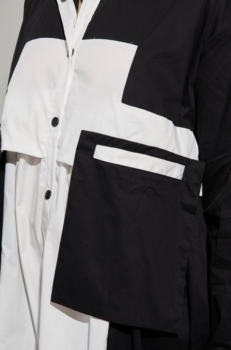 Close-up of the NOT FEELIN IT PARACHUTE MIDI DRESS featuring a black and white color-block design. This dress, inspired by windbreakers, showcases black buttons and large geometric panels, including a prominent rectangular flap on the front, creating a bold, contrasting pattern. 7