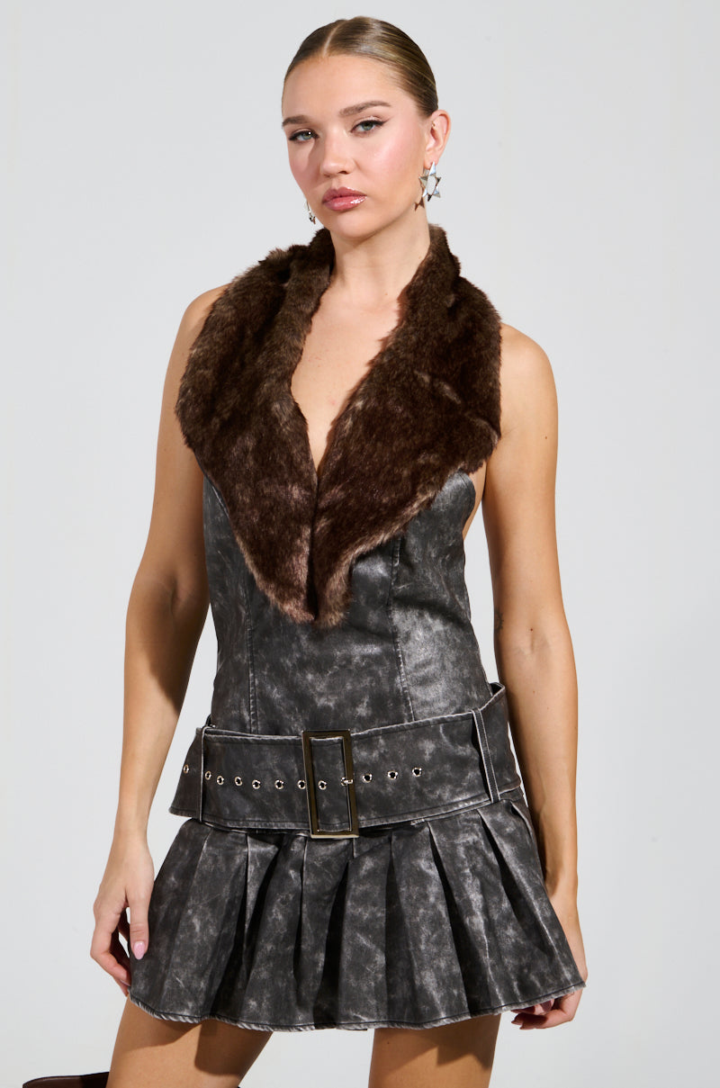 The individual is wearing the STEPPING OUT PU FUR TRIM MINI DRESS in gray, which features a brown fur collar and a belted waist. Star-shaped earrings add sparkle to the pleated skirt, standing out against the plain background.