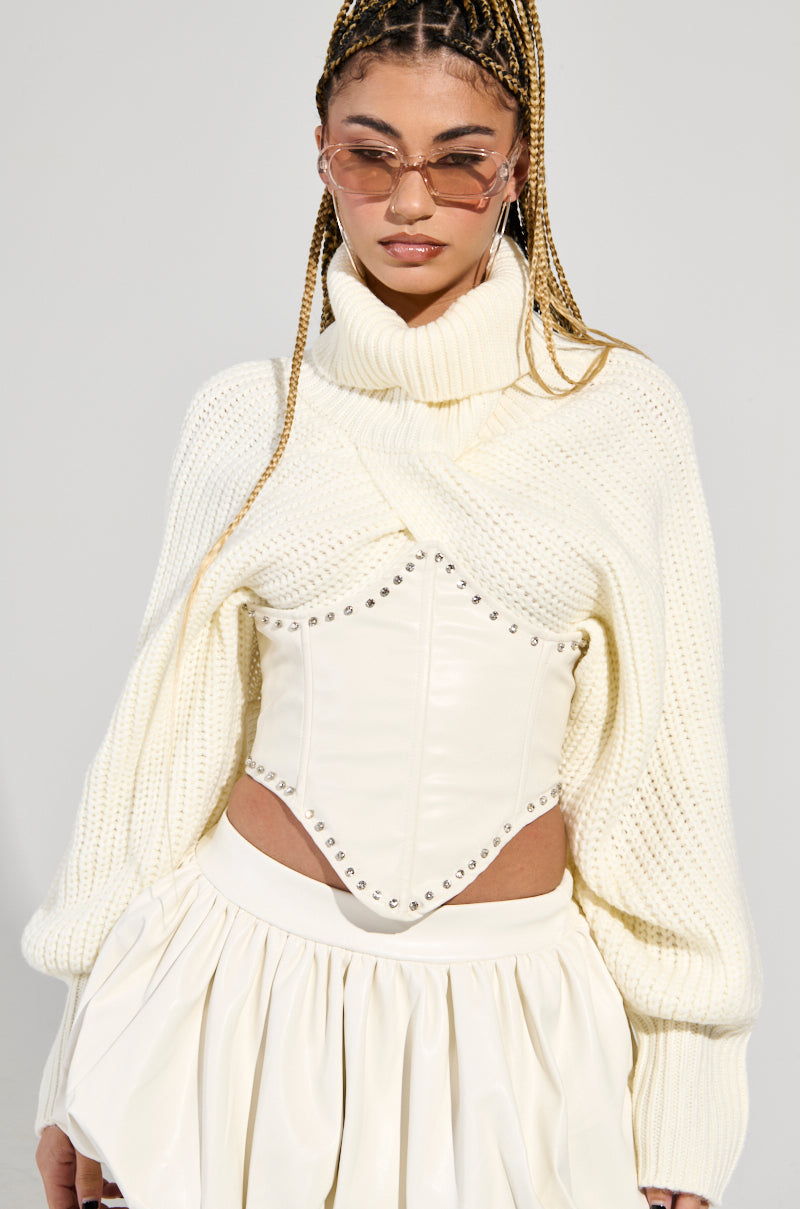 A person is dressed in a white knit turtleneck sweater paired with the PUT ME ON THE POSTER SNATCHED BELT and a white skirt. They have long, braided hair and are wearing sunglasses, set against a plain background that highlights their fashionable outfit.