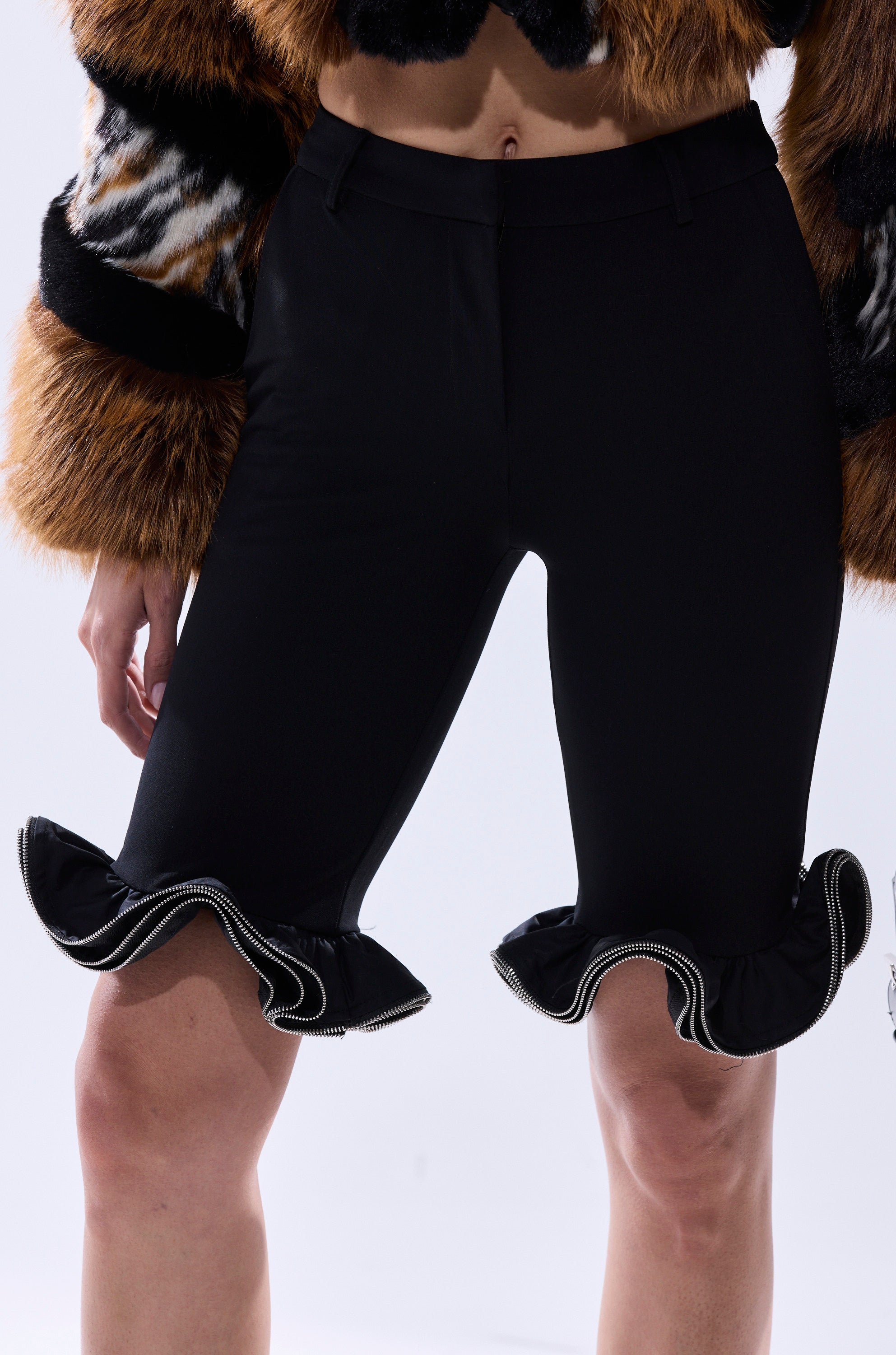 A person wearing the DAINTY DETAILS RUFFLE HEM TAILORED SHORT and a cropped faux fur jacket with brown, black, and white patterns. The image is cropped to show only the lower torso and upper legs.
