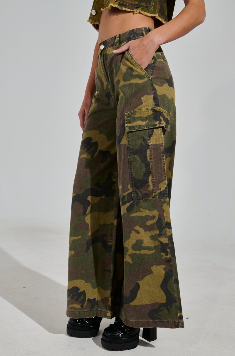 Someone wearing "RIDE WITH ME CAMO WIDE LEG PANT" and black chunky shoes stands against a plain backdrop.