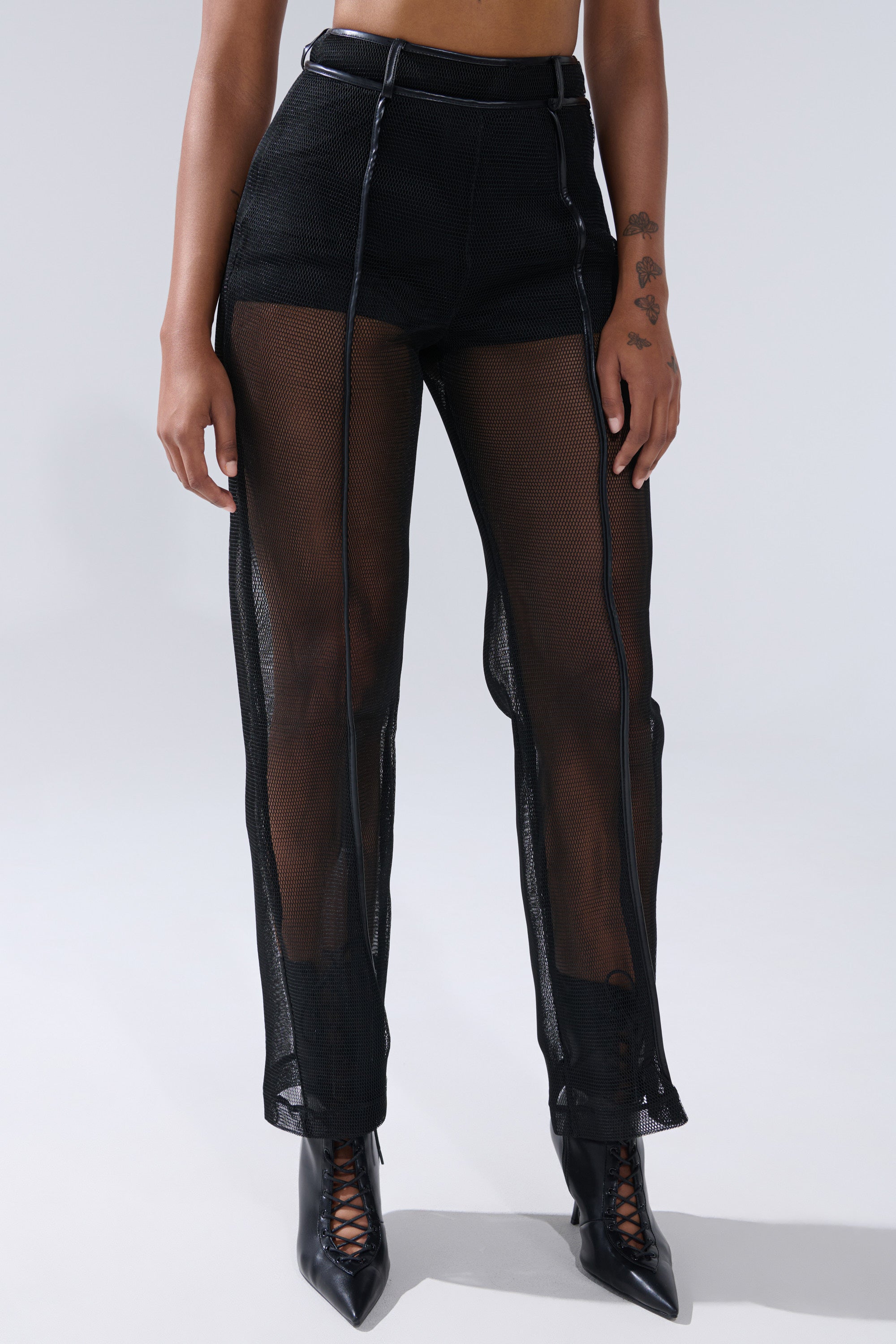The lower torso and legs are shown wearing the ONE TO WATCH MESH TROUSER—high-rise, sheer black mesh with visible seams and faux leather trim—paired with black lace-up pointed-toe boots. 1