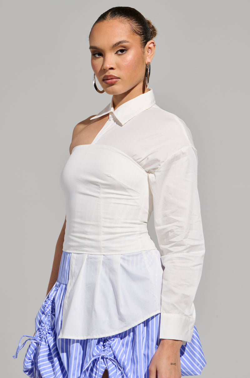 A person confidently models the DONT LOOK AT ME ASYMMETRICAL POPLIN BLOUSE, featuring a chic single sleeve design. They pair it with a mixed blue and white striped skirt, accessorize with hoop earrings, have their sleek hair pulled back, and pose against a plain gray backdrop.