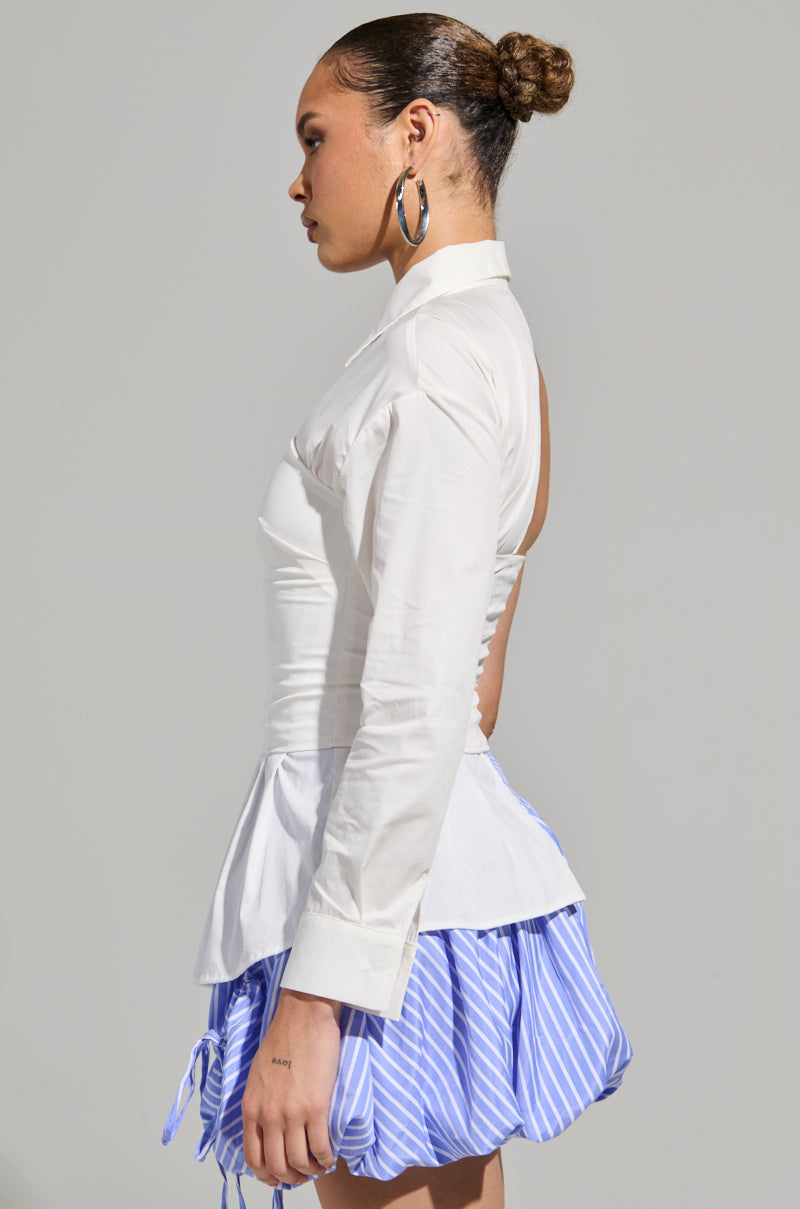 A person with a bun hairstyle is wearing the "DONT LOOK AT ME ASYMMETRICAL POPLIN BLOUSE," paired with a blue and white striped skirt. Viewed in profile against a simple backdrop, they are looking to the left and accessorized with hoop earrings.