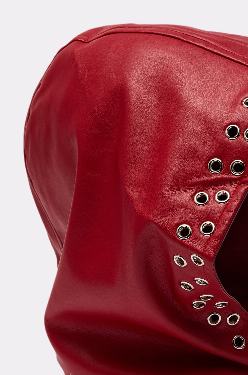 Close-up of the BUCKLE UP PU HEADSCARF, an oversized red leather hood with metal eyelets in curved lines, shown against a plain light background. 6