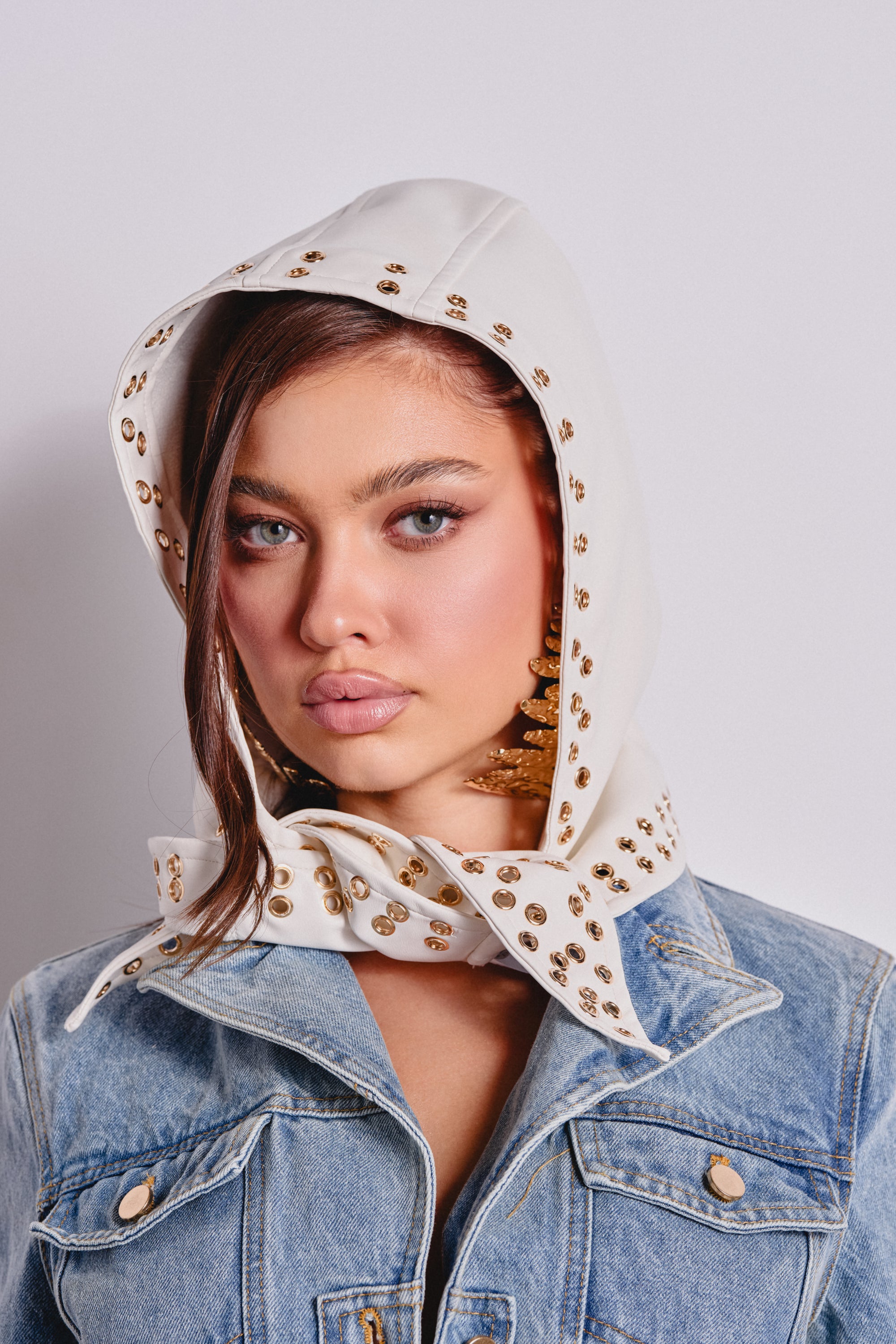 Young woman with blue eyes wears the THAT GURL PU GROMMET HEADSCARF, styled with a denim jacket and large gold earrings for a chic streetwear look. 0
