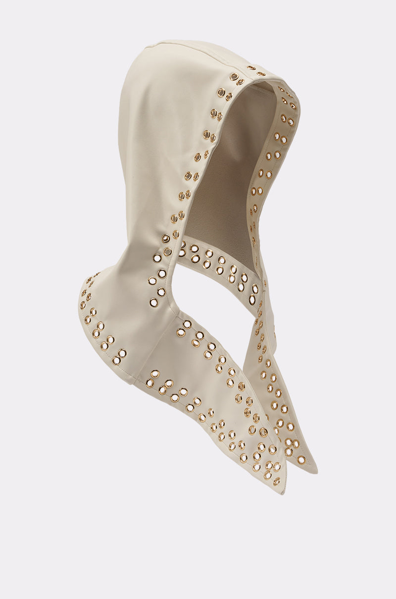 The THAT GURL PU GROMMET HEADSCARF features a cream color, hooded design, and gold grommet detailing along the edges and openings—a bold streetwear accessory against a light background. 2