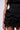 Close-up of a person wearing the black, sleeveless FUN N FLIRTY RUFFLED POPLIN MINI DRESS featuring multiple ruffled layers around the waist and bottom. The curve-hugging fit is highlighted against a plain background.