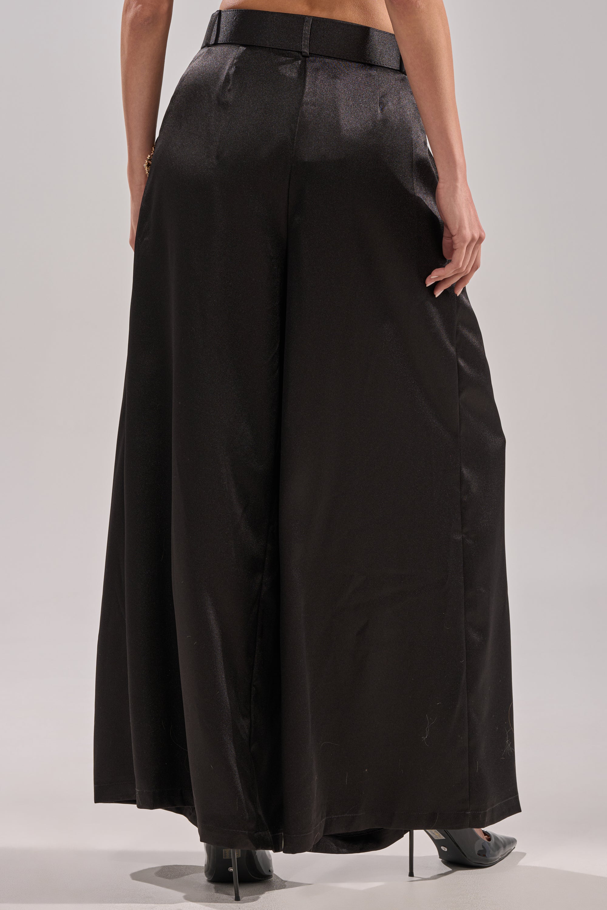 A person is shown from the waist down wearing the AFTER DARK TROUSER satin wide-leg pants and black high heels, standing against a plain light background.