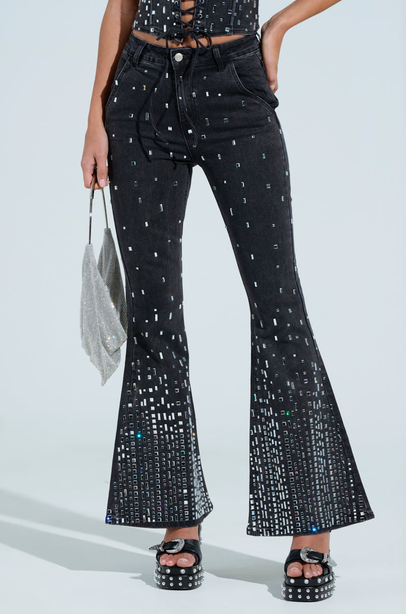 Wearing the POPSTAR BLACK DENIM PANT WITH RHINESTONE, this chic outfit showcases a silver sequin pattern, complemented by a stylish silver handbag. The mid-rise pants pair perfectly with platform shoes featuring silver studs, all set against a neutral backdrop.