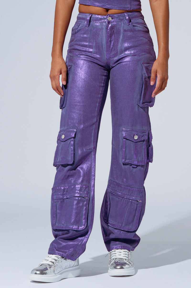 Person wearing THE POWER OF LOVE DENIM CARGO PANT in high-rise wide-leg purple, featuring multiple pockets, paired with metallic silver sneakers, standing against a plain background. Their face is not visible in the image. 0