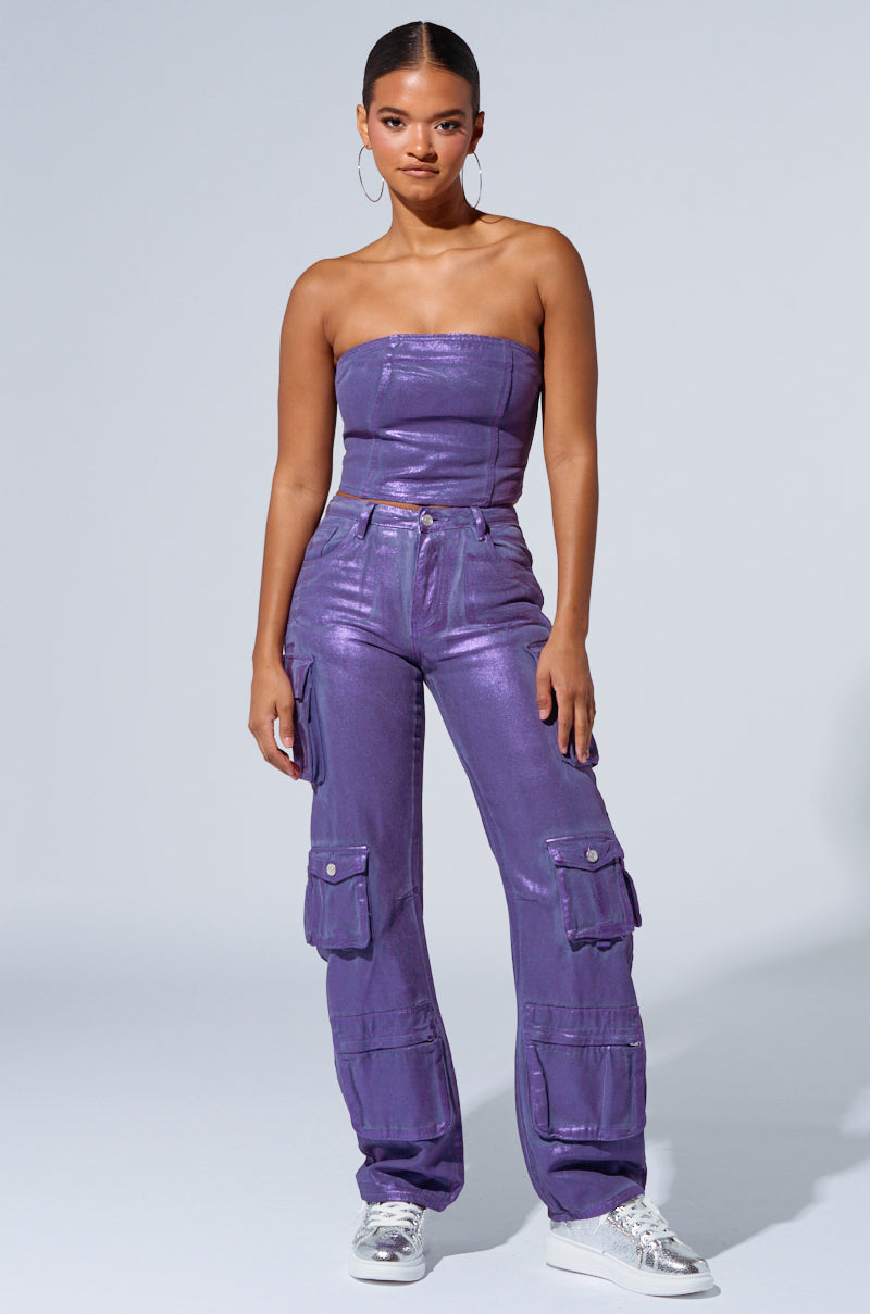 A woman stands against a plain background wearing a shiny, metallic purple strapless top and THE POWER OF LOVE DENIM CARGO PANT in matching high-rise wide-leg style. She completes the look with large hoop earrings and metallic silver sneakers, with her hands resting on the sides of her thighs. 4