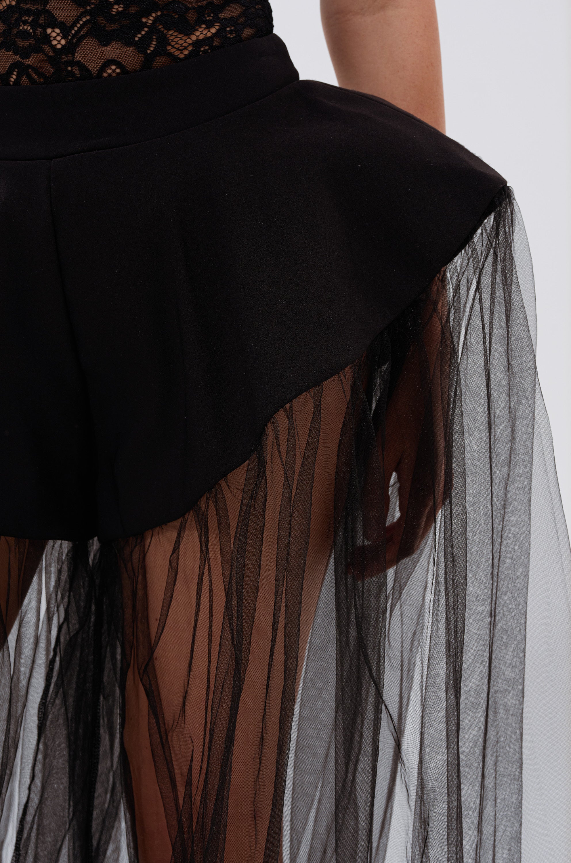 Model showcases the ALL OF THE DRAMA TULLE PANTS—a high-waisted black style with a sheer, pleated tulle overlay—paired with lace detail from the waist down against a plain background, capturing avant-garde fashion.