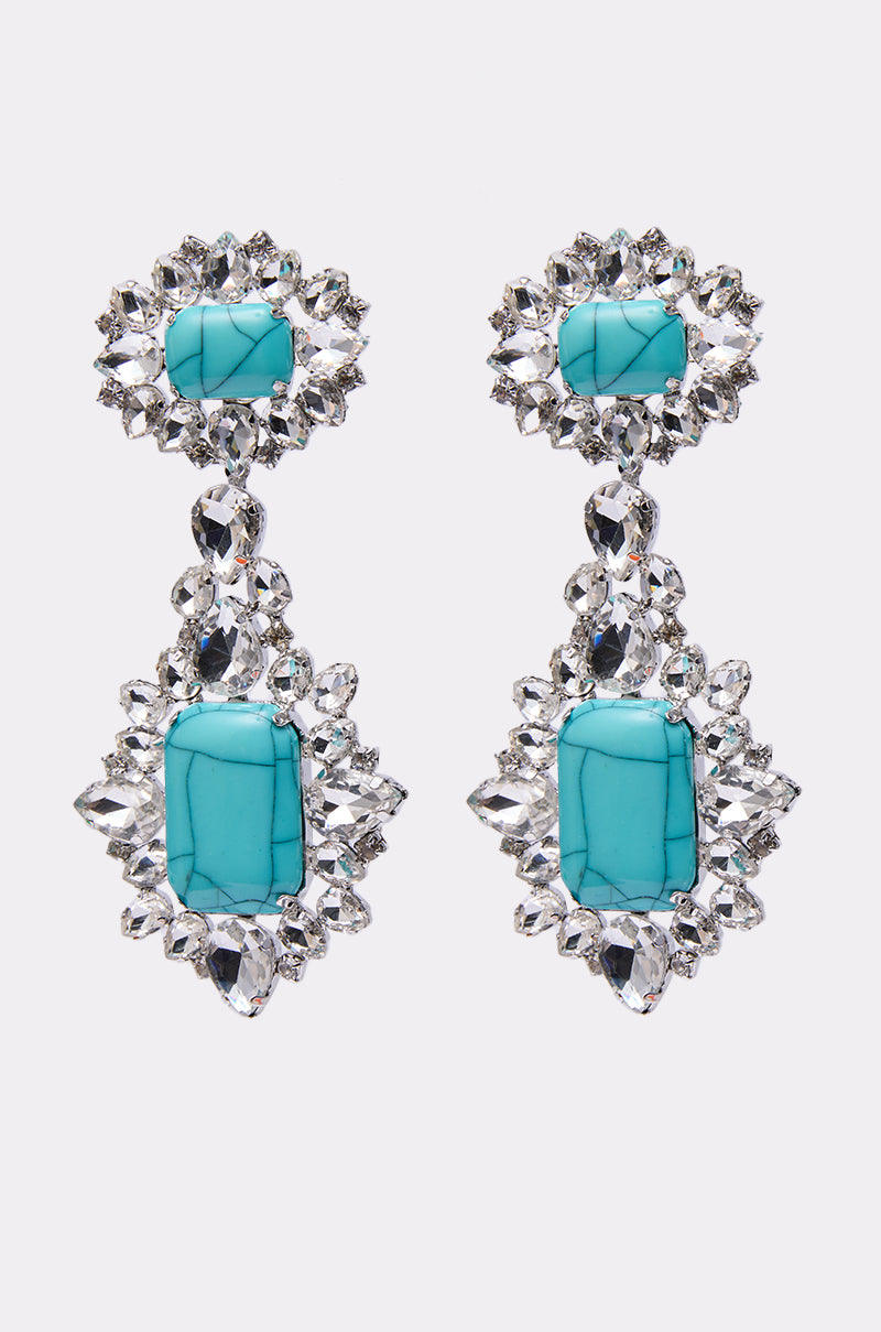 The TOTALLY TURQ EARRING features large marbled turquoise stones at the center, accented with sparkling rhinestones on a silver setting, shown against a plain white background.