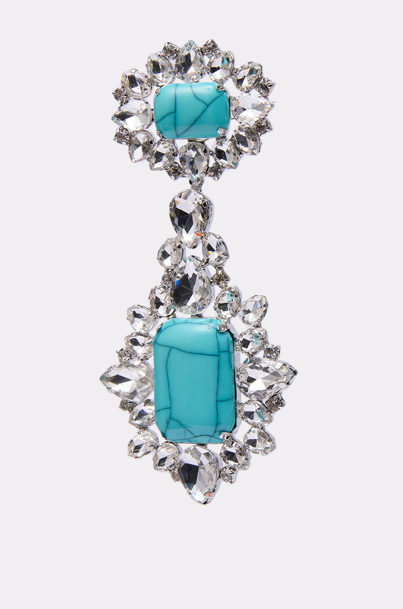 The TOTALLY TURQ EARRING is a statement dangle earring with two vertically linked rectangular turquoise stones, each framed by rhinestones and set in gleaming silver metal.