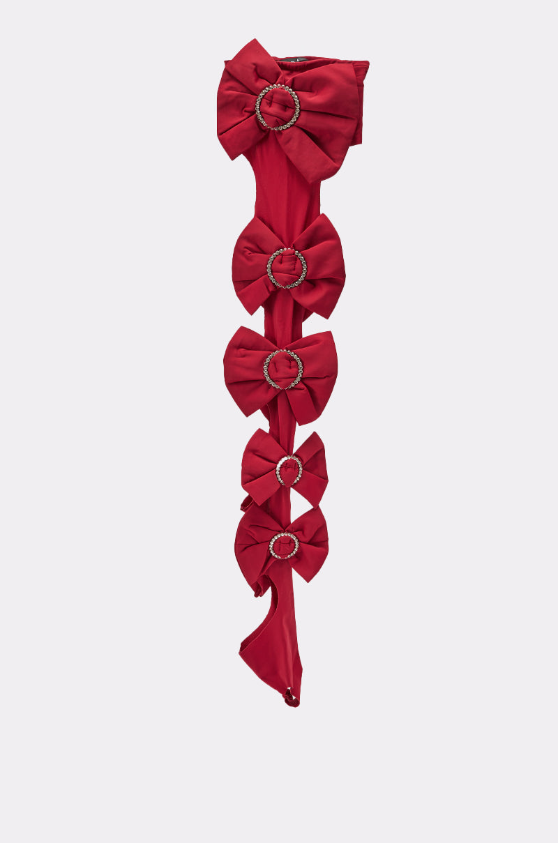 The LOVES ME STIRRUP STOCKINGS are long red stockings featuring five large bows arranged vertically, each bow secured with a jeweled clasp at the center, displayed against a plain light background. 2