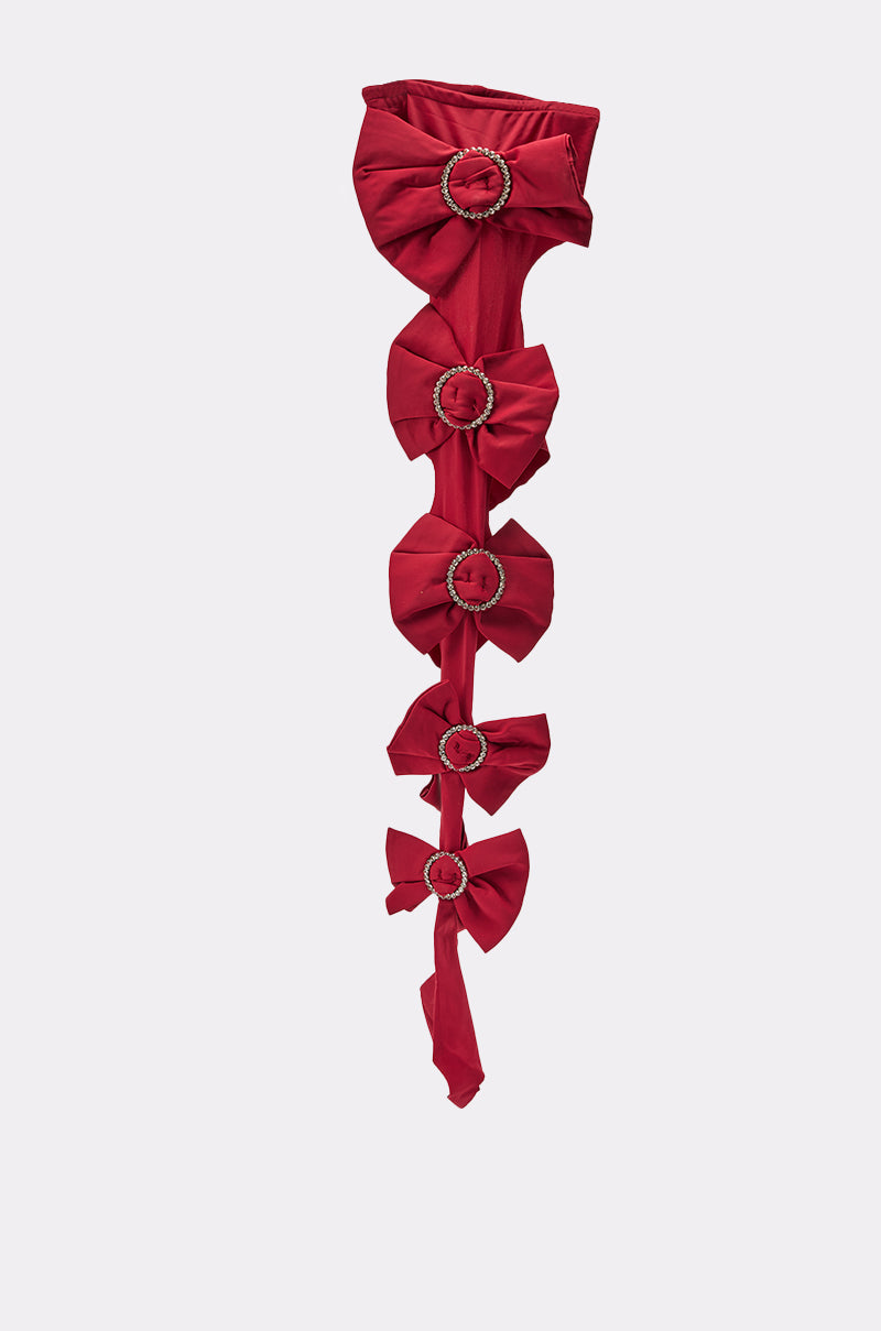 LOVES ME STIRRUP STOCKINGS: Red fabric stockings featuring five large bows, each with a circular jeweled buckle at the center, displayed against a plain light background. 3
