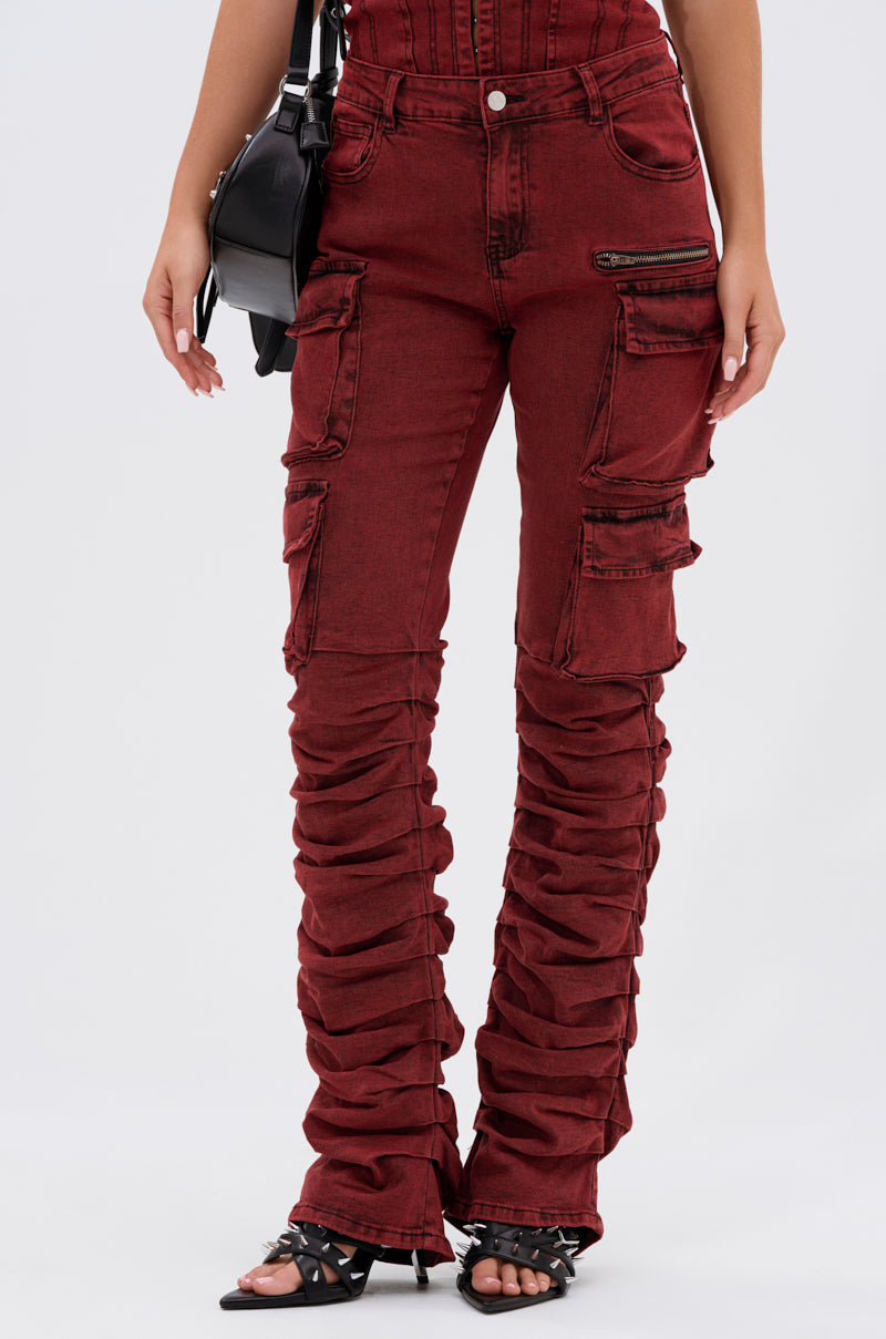 A person wears the IT GETS EASIER STACKED CARGO PANT IN BURGUNDY—high-rise streetwear denim with multiple pockets and ruched legs—styled with black heeled sandals and a black handbag.