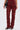 A person wears the IT GETS EASIER STACKED CARGO PANT IN BURGUNDY—high-rise streetwear denim with multiple pockets and ruched legs—styled with black heeled sandals and a black handbag.