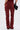 Facing away, a person models the IT GETS EASIER STACKED CARGO PANT IN BURGUNDY—high-rise streetwear denim with back pockets, stacked cargo details, and flared bottoms—paired with a small black purse for a bold statement.