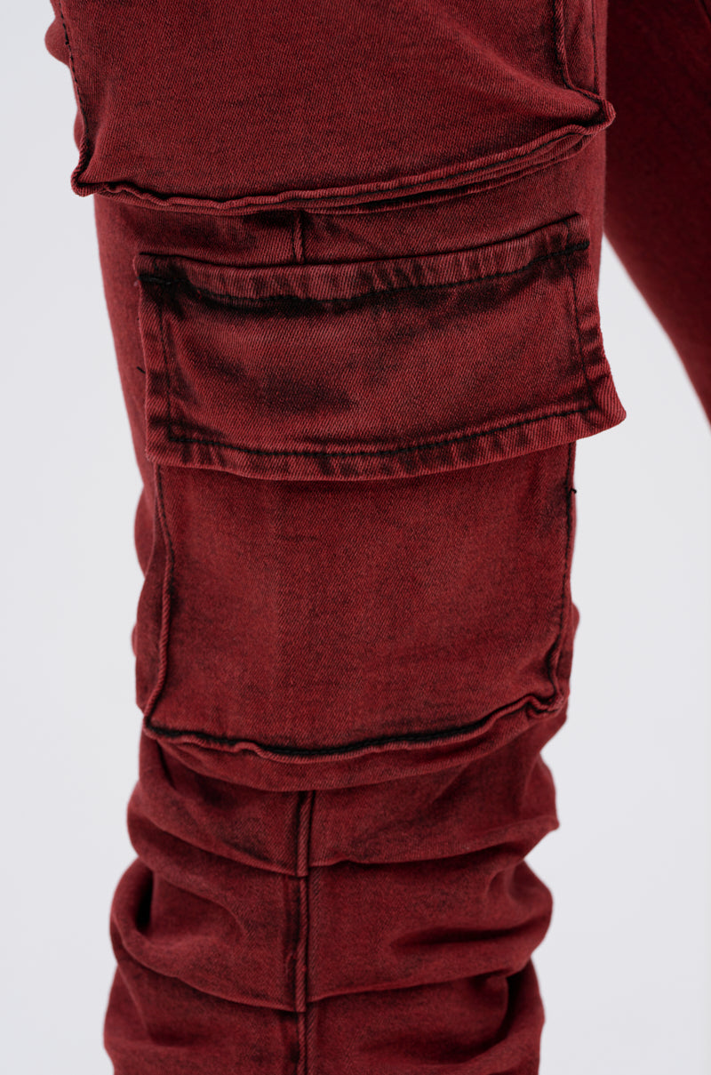 Close-up of the IT GETS EASIER STACKED CARGO PANT IN BURGUNDY, showcasing a large flap pocket with visible dark seams and distressed details against a plain light background.
