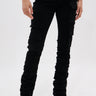 A person wears DOUBLE VISION VINTAGE WASH DENIM PANT, featuring a high-rise fit, multiple cargo pockets, and leg ruching, paired with pointed black shoes, standing against a plain white background.