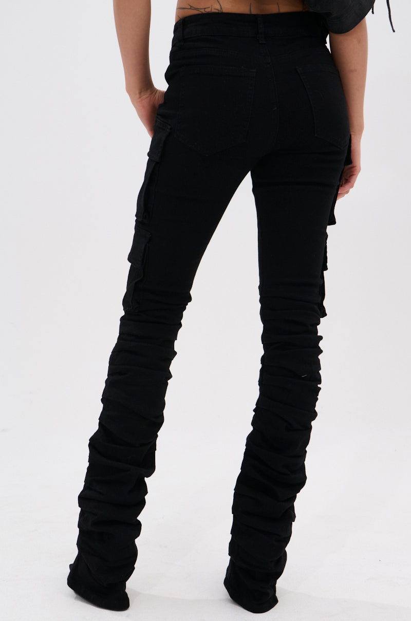 A person stands facing away, wearing the DOUBLE VISION VINTAGE WASH DENIM PANT, featuring a sleek high rise fit and cargo pockets, paired with black shoes against a plain white background.